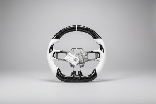 A forged carbon fiber steering wheel with Nappa perforated leather, displayed on a flat surface.