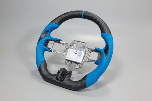 A aftermarket carbon fiber steering wheel for a Ford Mustang, featuring blue and black color with carbon fiber texture.