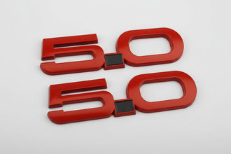A set of two red metal side fender badges for a Mustang, featuring the number '50'.