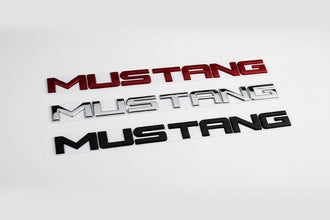 A set of Mustang decklid lettering in chrome, red, and black finishes.