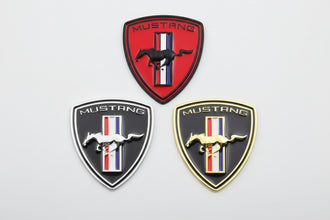 A set of three Mustang Tri-bar Shield Badges in red, black, and gold colors with a white background.
